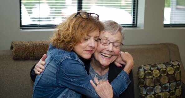 Two people sit next to each other on a couch and embrace.